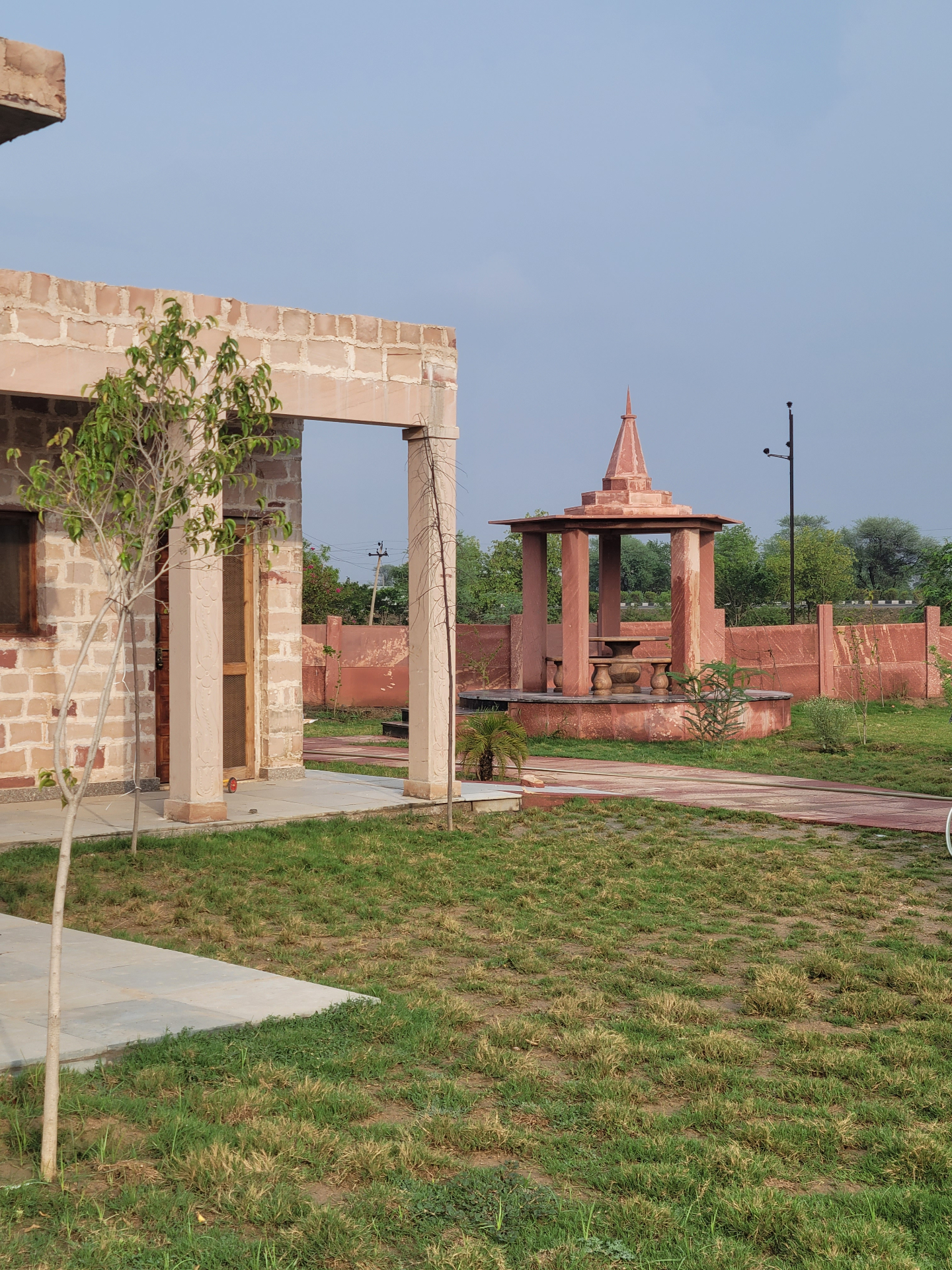 Red-sandstone Ayurveda retreat at dawn in rural Rajasthan with neem trees and a brass water pot